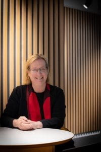 Professor Evelyn Welch at a table with black jacket and red scarf against low lit background
